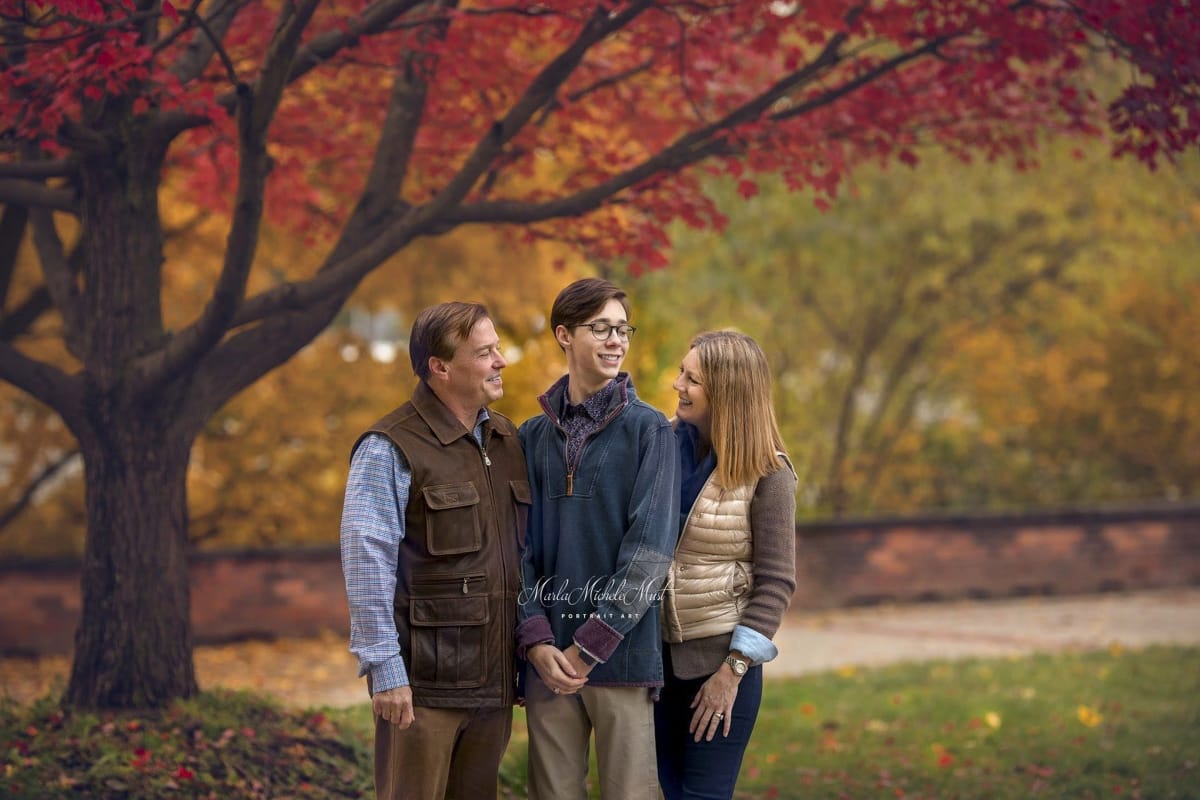 A fall family photoshoot of a mother and father looking lovingly at their teenage son