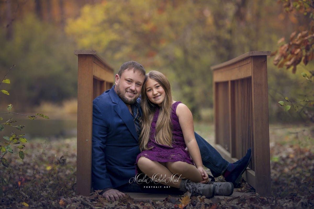 A lovely fall father and daughter family portrait. The father and the daughter sitting on a bridge near Detroit, MI