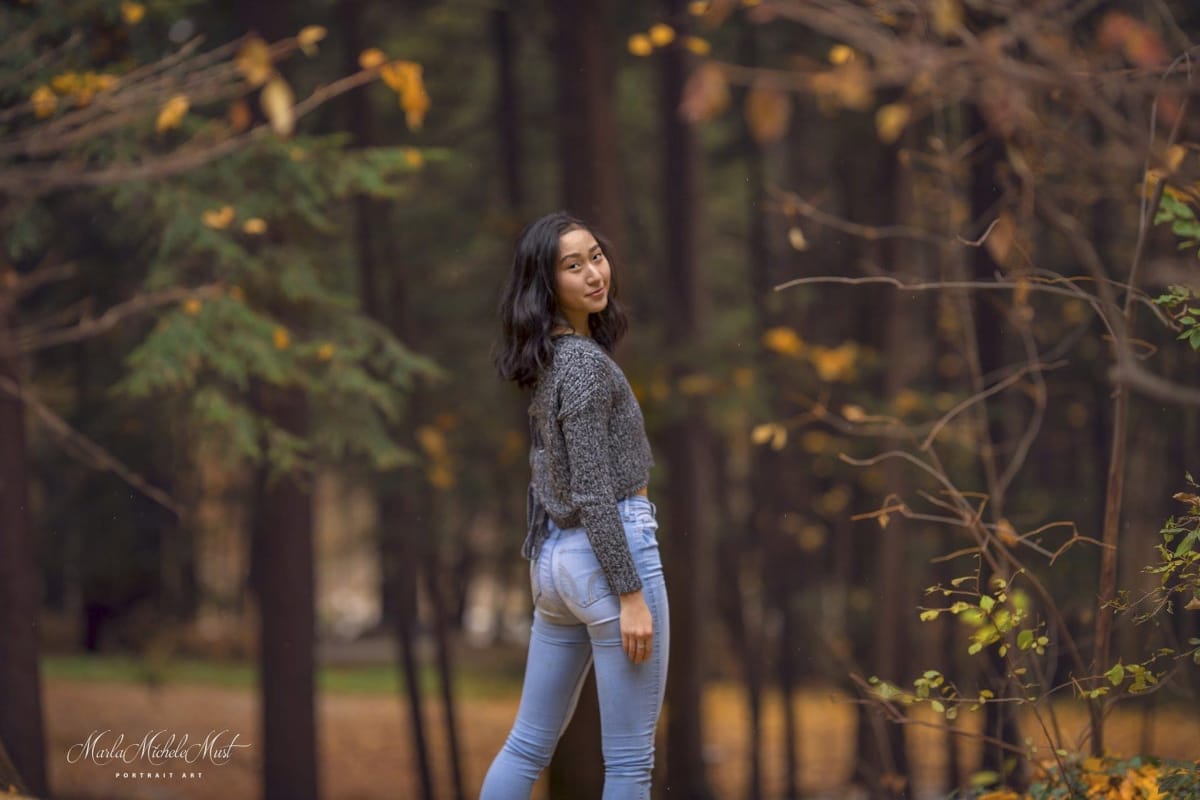 A high school senior looks over her shoulder in a Michigan forest as part of her high school graduation photoshoot