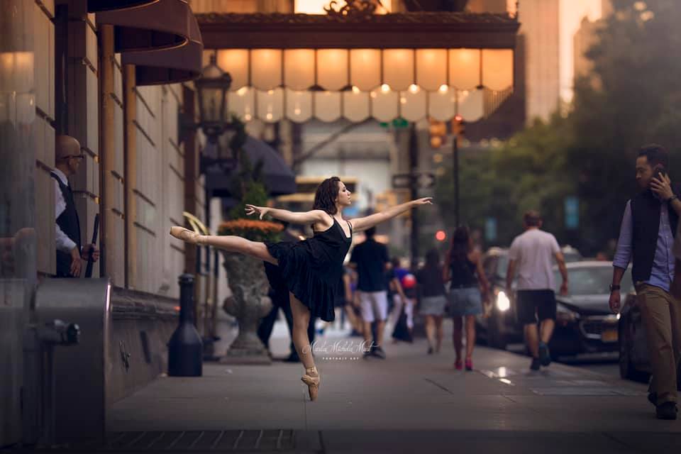 Dancer embodies poise in an arabesque pose, photographed by a skilled Detroit-based photographer on a busy Michigan metropolitan sidewalk..