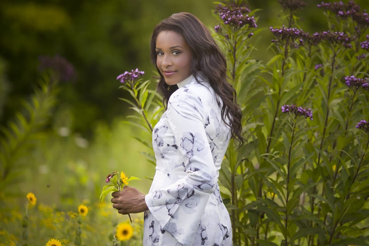 A young woman picks flowers in a Michigan meadow - captured by a talented Detroit photographer during a senior portrait session.