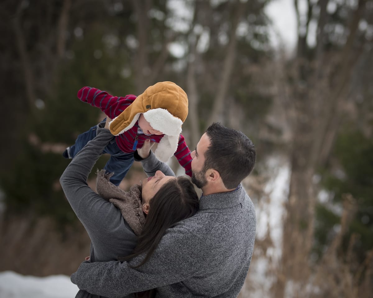 Winter family photoshoot of a mother and father holding their baby in the air in the snowy Michigan wilderness