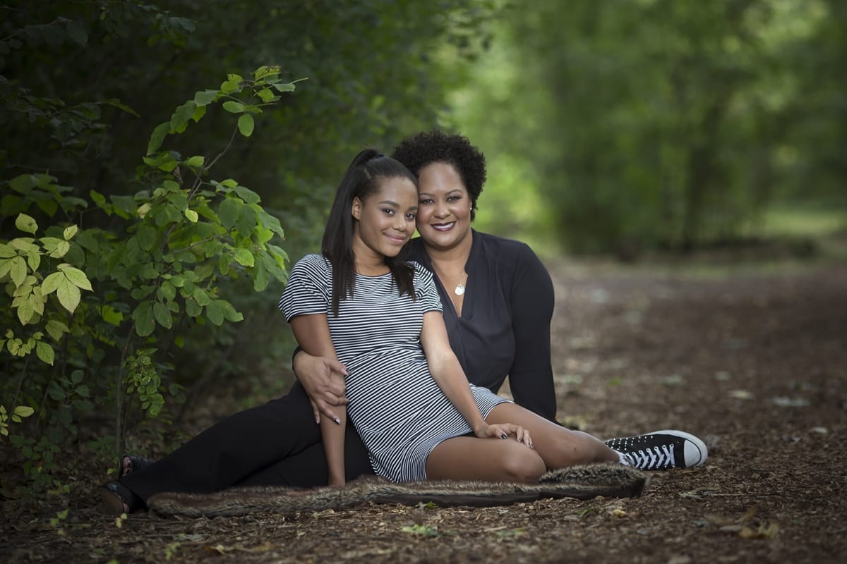 A mother and daughter gracefully sit next to each other on a forest path near Detroit, MI for a family photo