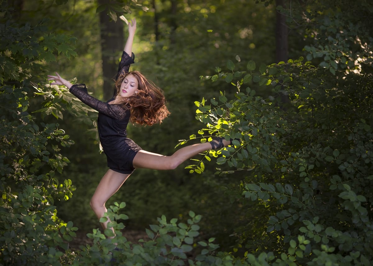 Dancer strikes a powerful pose, one leg extended, both arms gracefully extended, showcasing strength and agility with seamless flow, expertly captured in a forest landscape by a Detroit-based photographer.