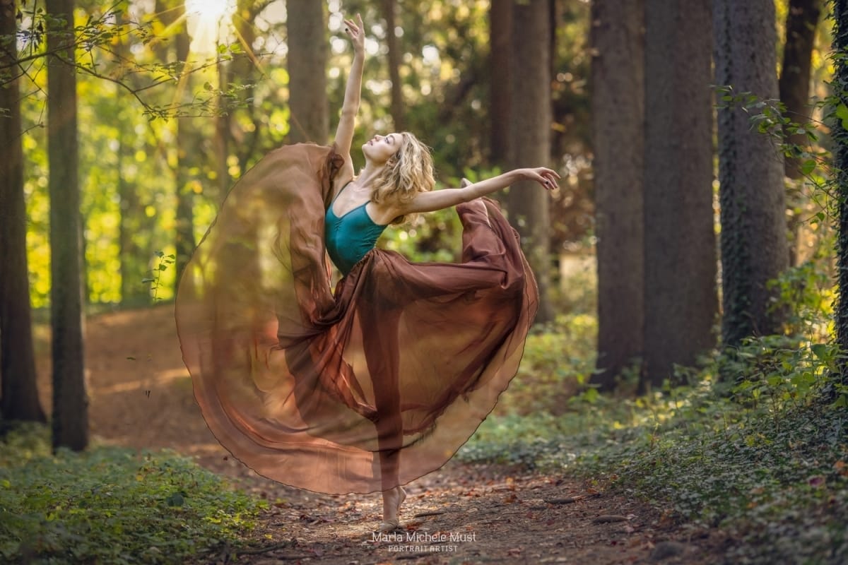 A dancer extends her leg in a poised partial arabesque pose while wearing a flowing skirt in the forest, captured by a Detroit-based photographer.