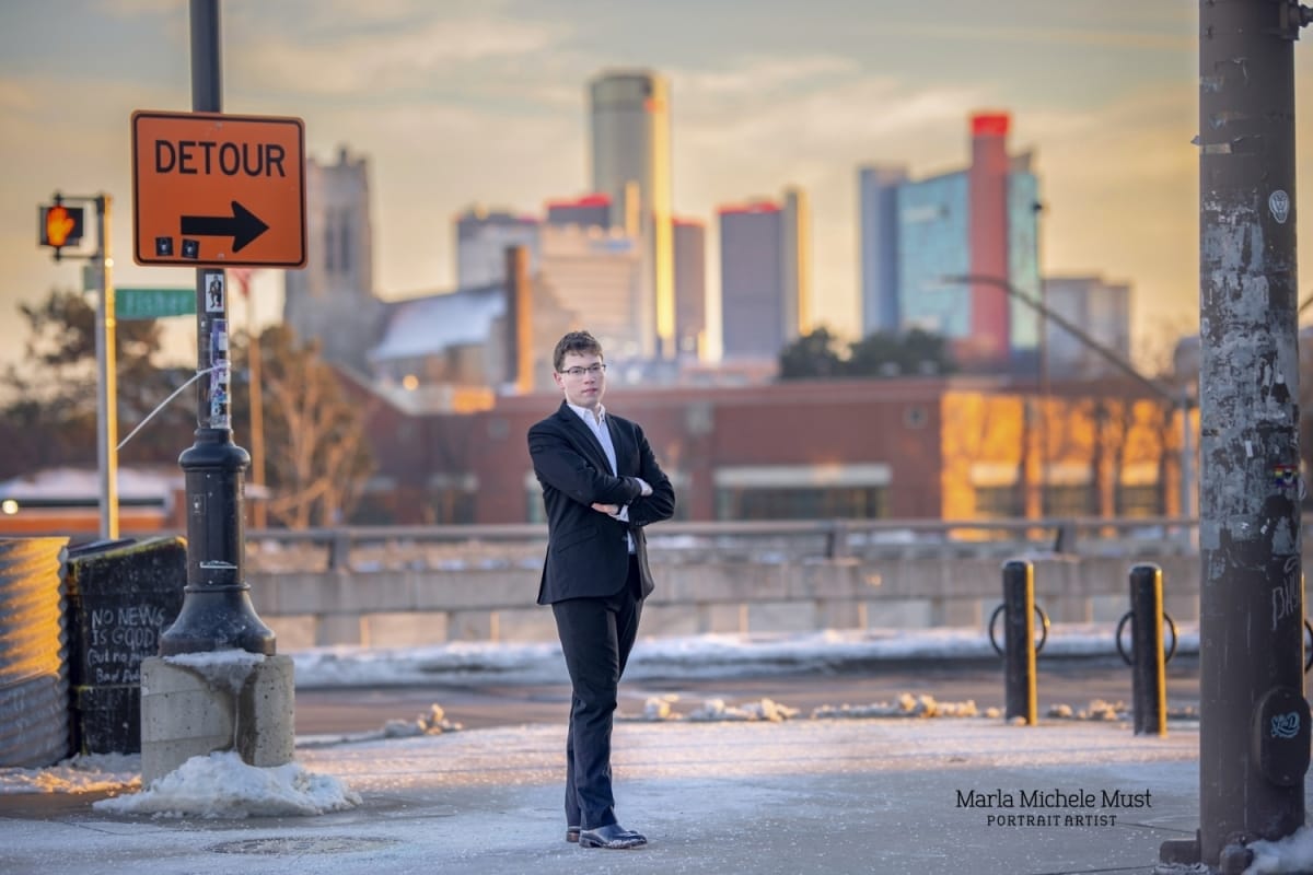 A high school student gazes confidently in suit, the sunset-lit Detroit skyline behind him, - A moment captured by a Detroit photographer.