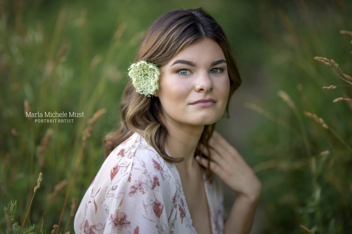 A closeup senior portrait of a Michigan student - she holds her hand to her shoulder and has a flower in her hair.