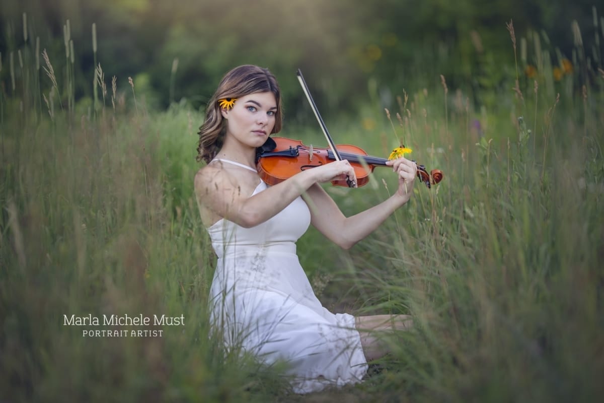 High school senior poses for her senior portrait in a Detroit field as she plays her violin