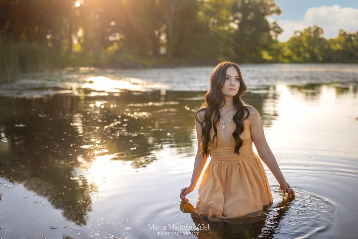 A high school student gazes confidently off camera as she wades in a Detroit-area lake, expertly captured by a skilled Detroit photographer during a senior portrait session