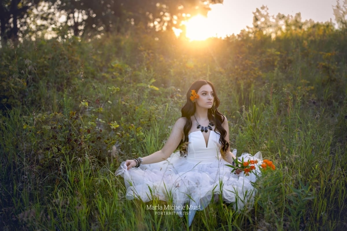 Girl in a floaty fairy-like white dress poses for her senior portrait in a Michigan meadow at sunset - captured by a skilled Detroit photographer.
