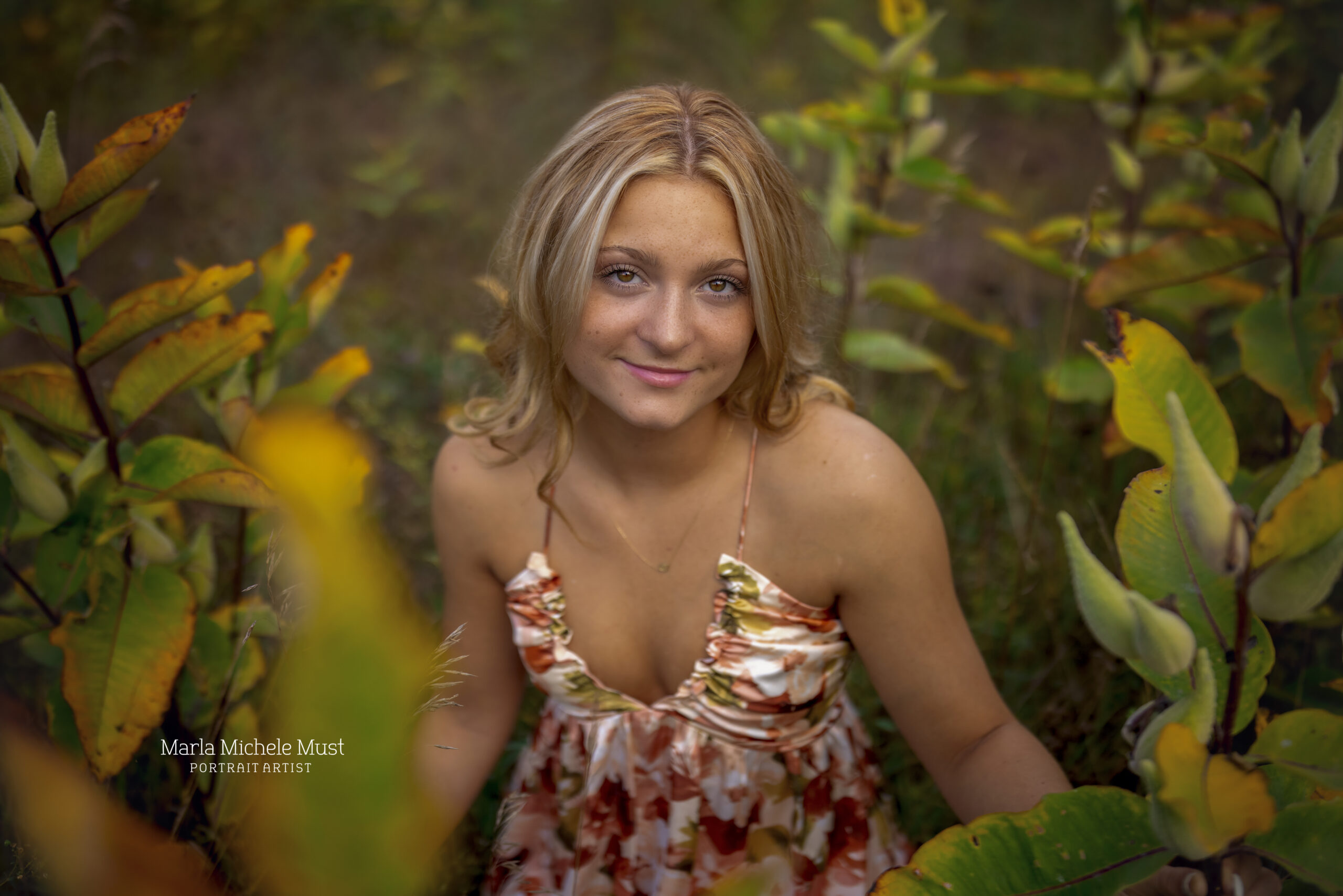 Girl in a red dress smiles at the camera for her senior pictures