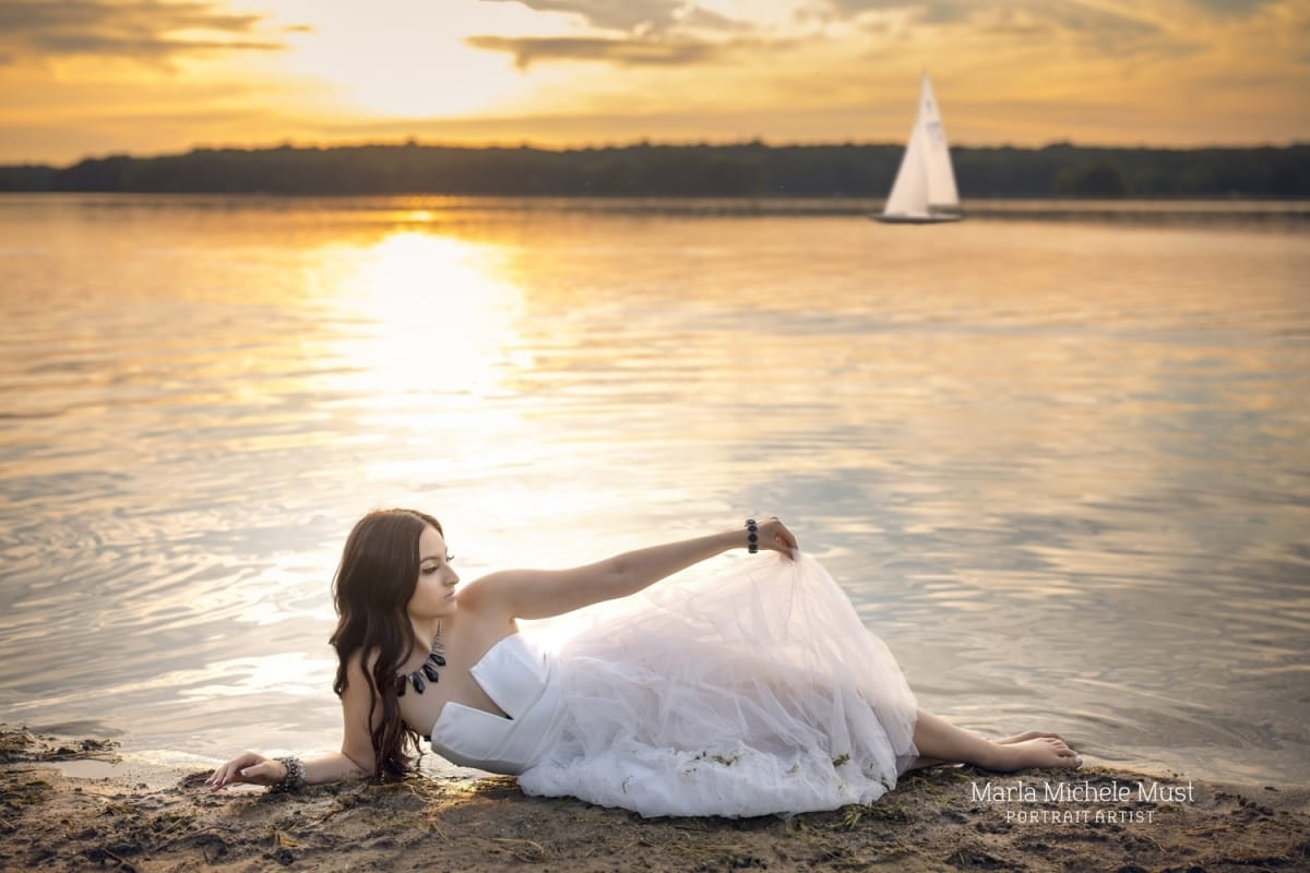 senior picture by great lake at sunset in white dress with sailboat in background