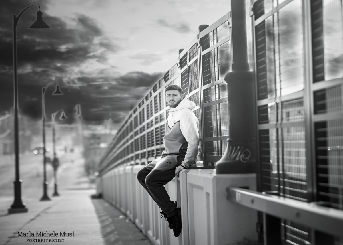 A high school senior poses for their graduation photoshoot by sitting on a Detroit bridge - styled in black and white by a Detroit senior portrait photographer.