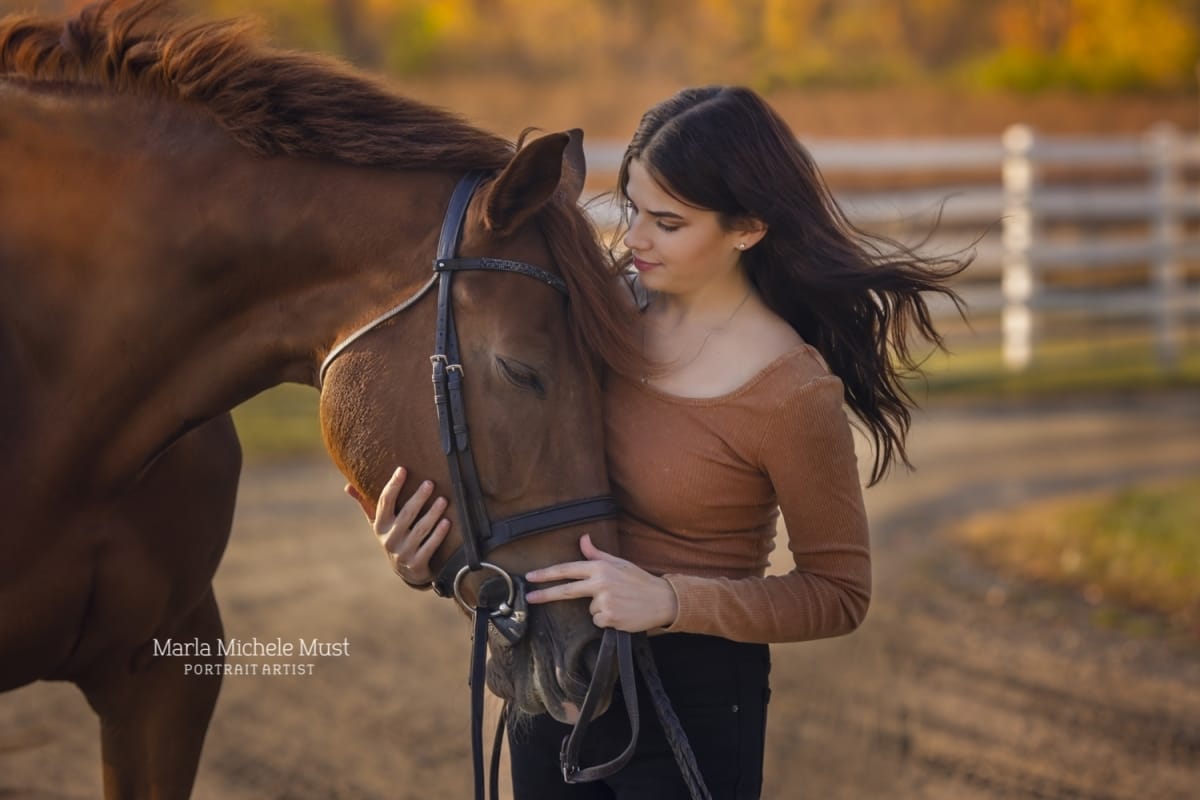 Portrait captured by a Detroit equine photographer, the peaceful owner holding her horse's head, surrounded by fall colors.