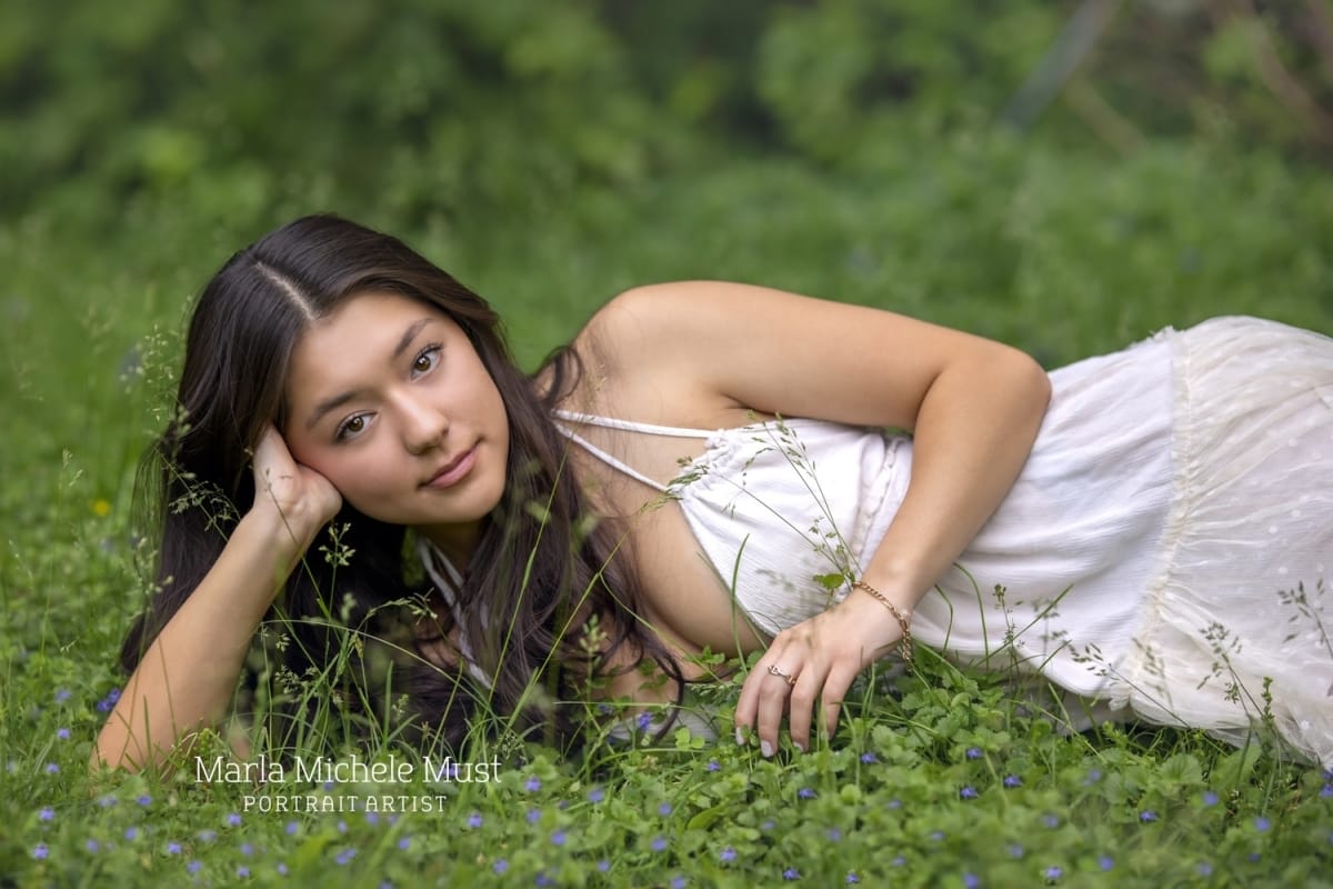 For her high school senior portrait, a girl poses on her side in a Detroit meadow.