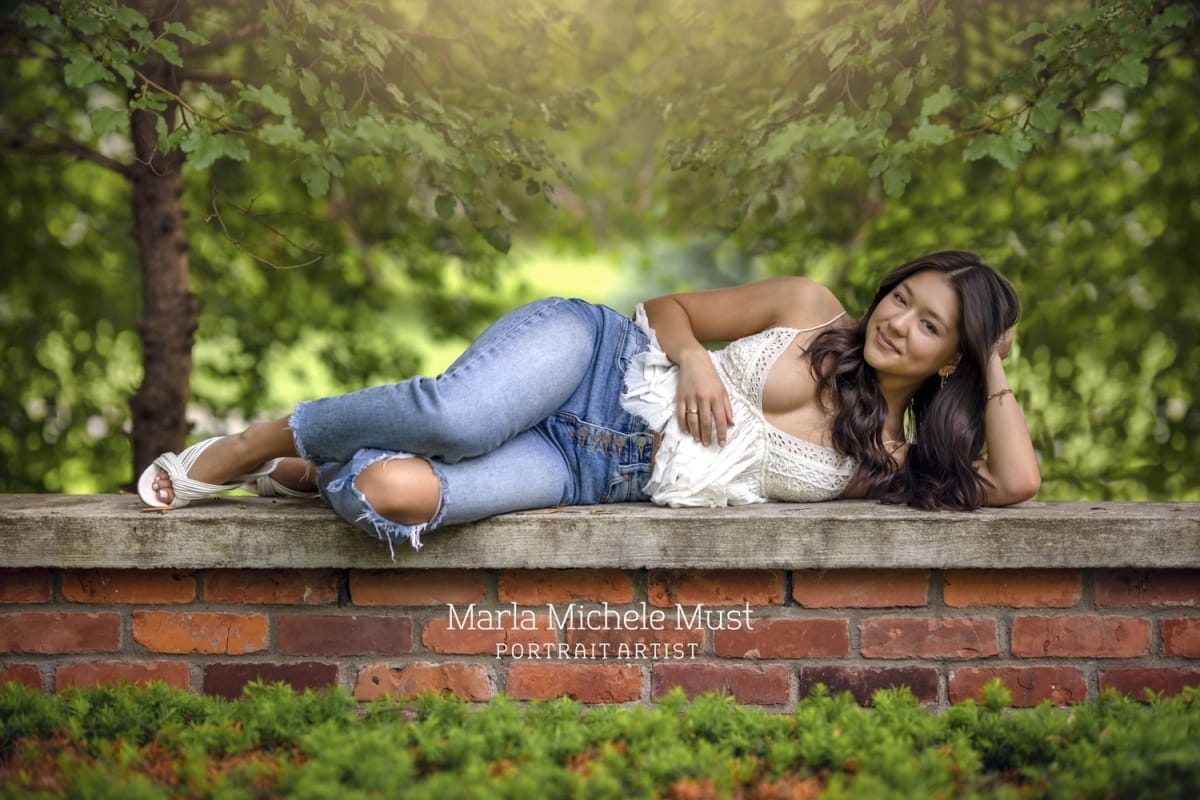 Senior lays on her side on a brick wall in a Detroit park as part of her high schools senior portrait session.