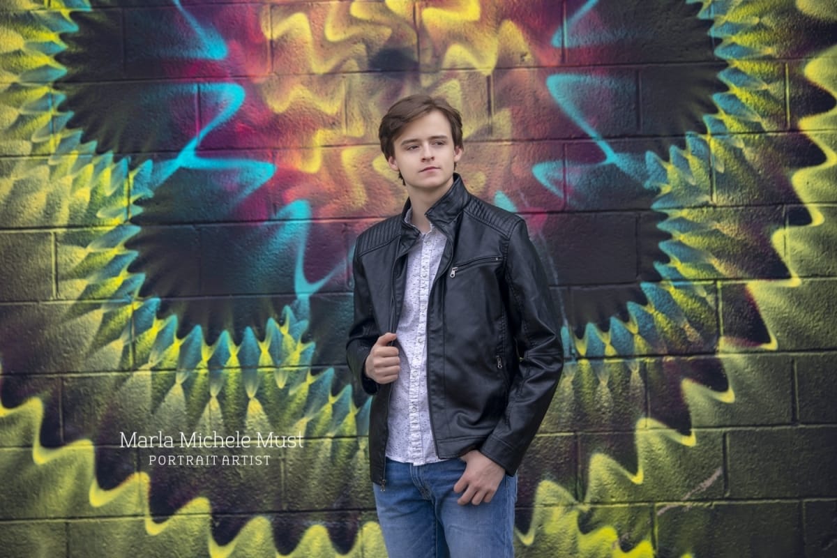 Senior portrait of a young man in front of a graffitied wall in downtown Detroit.