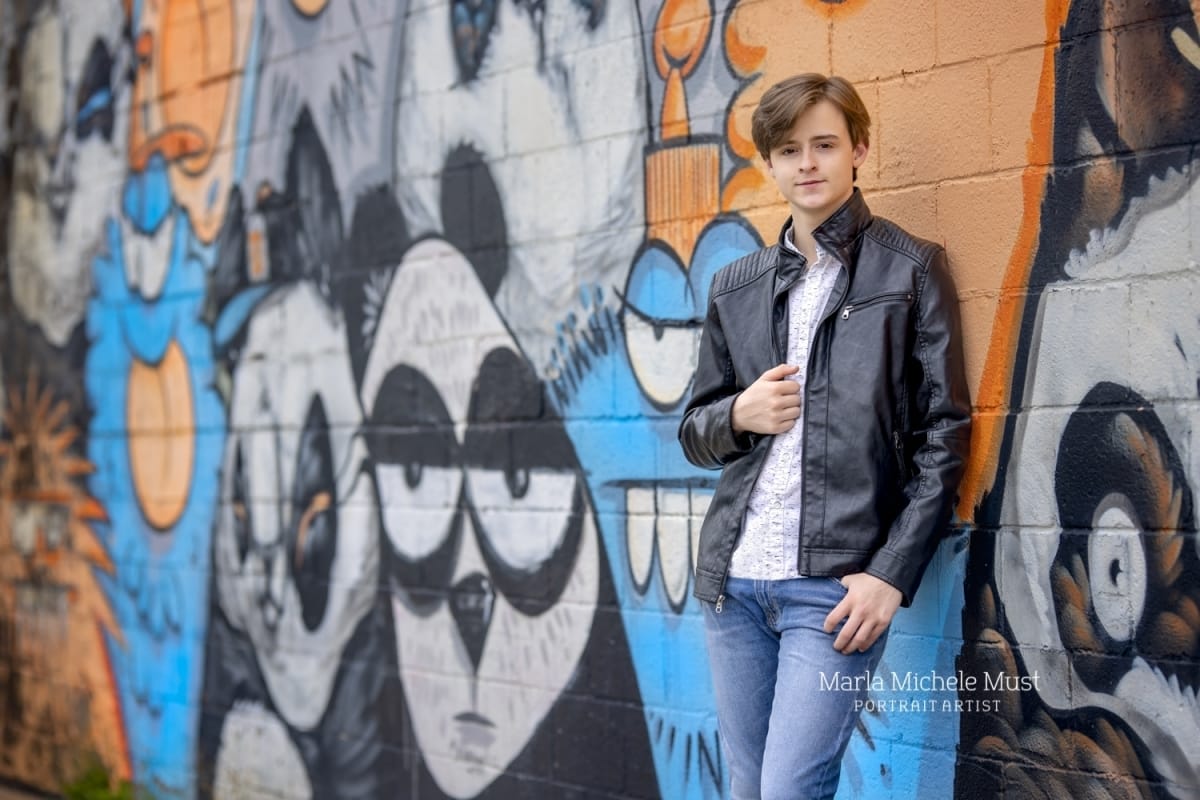 Edgy senior picture of a high school senior holding his leather jacket next to cartoon street art in downtown Detroit