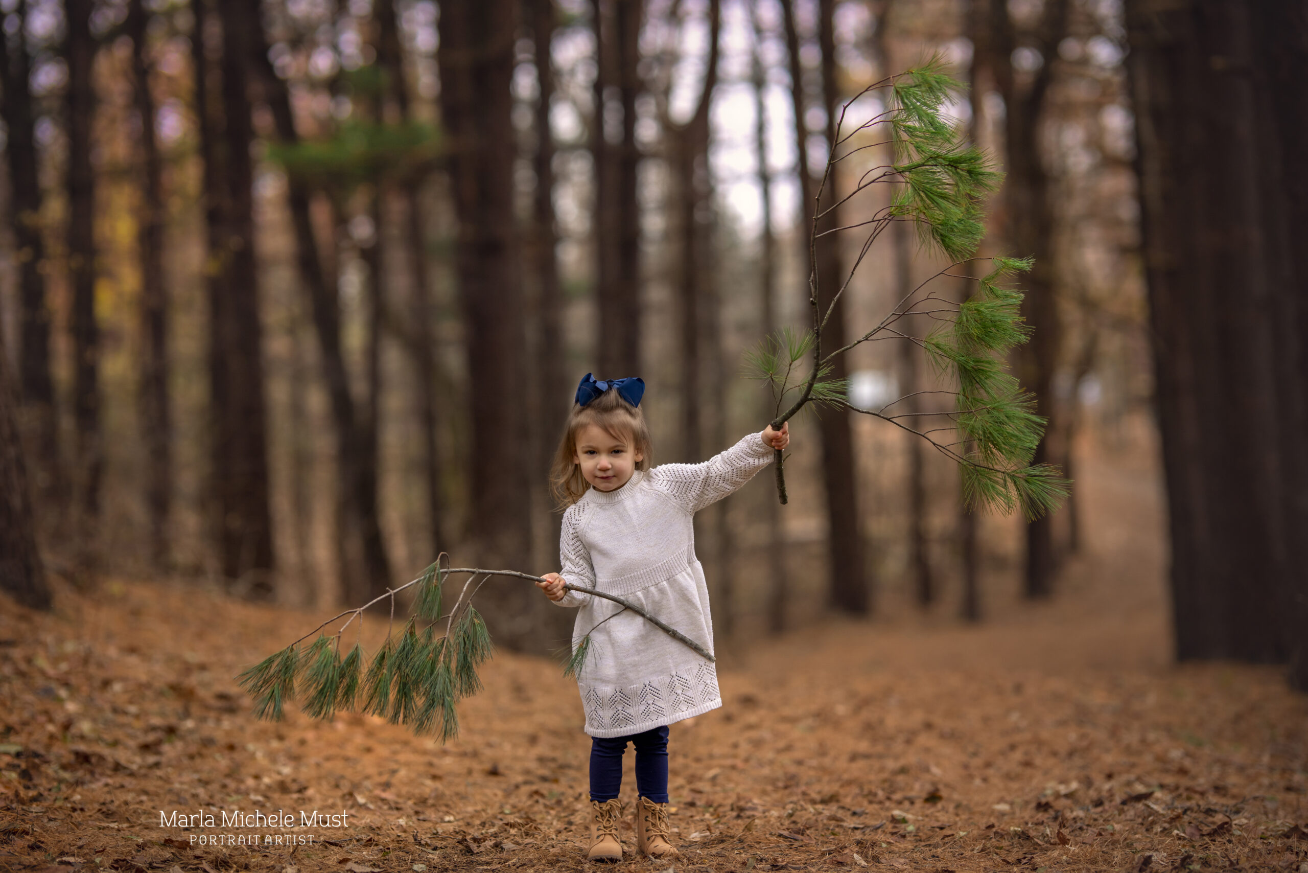 A young child walking through a bed of leaves in the forest while holding a branch somewhere near Detroit.