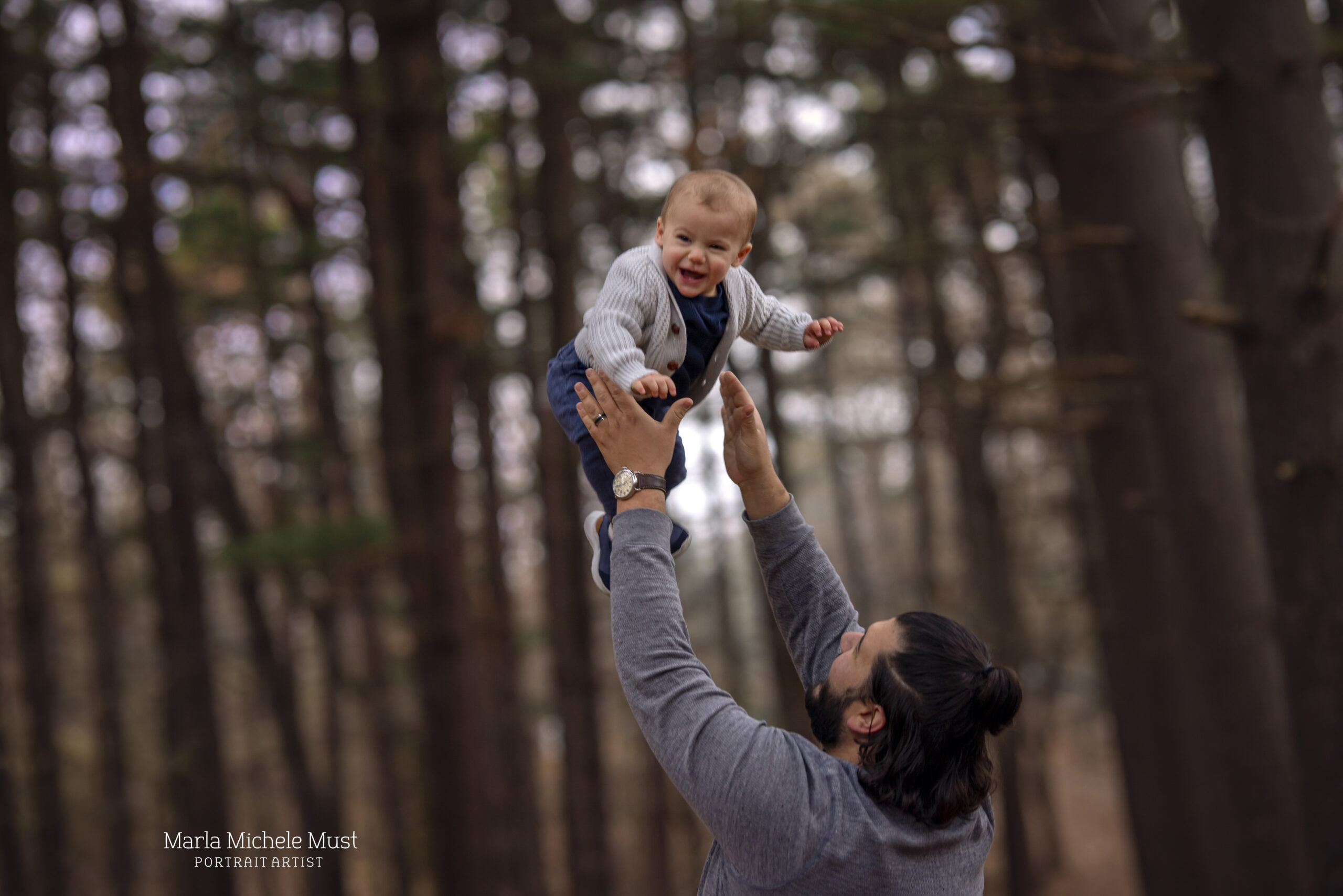 A fall portrait of a man holding up his baby while the baby laughs.