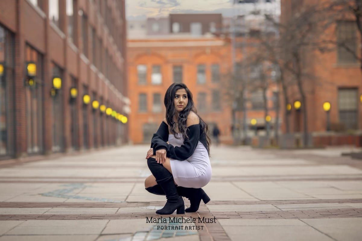 Young female graduate poses while crouched down on a downtown Detroit street for her high school senior portrait