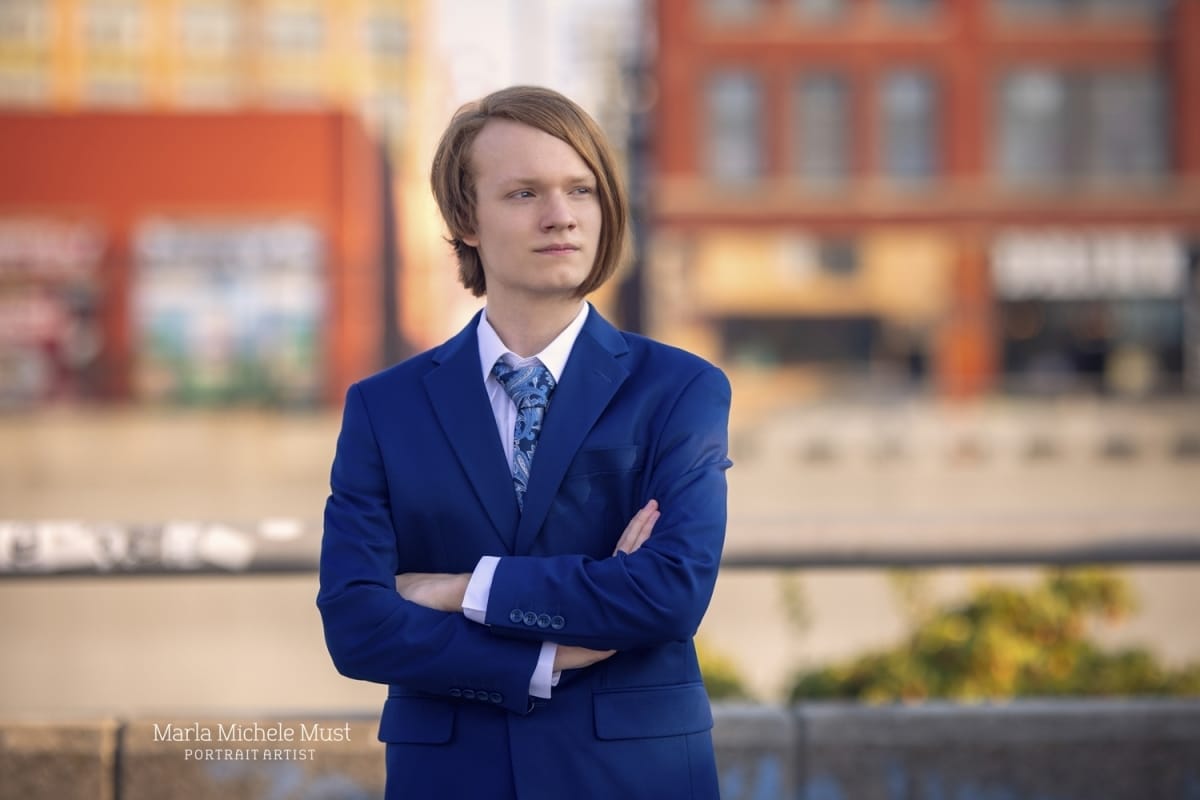 senior picture in suit in front of downtown Detroit buildings