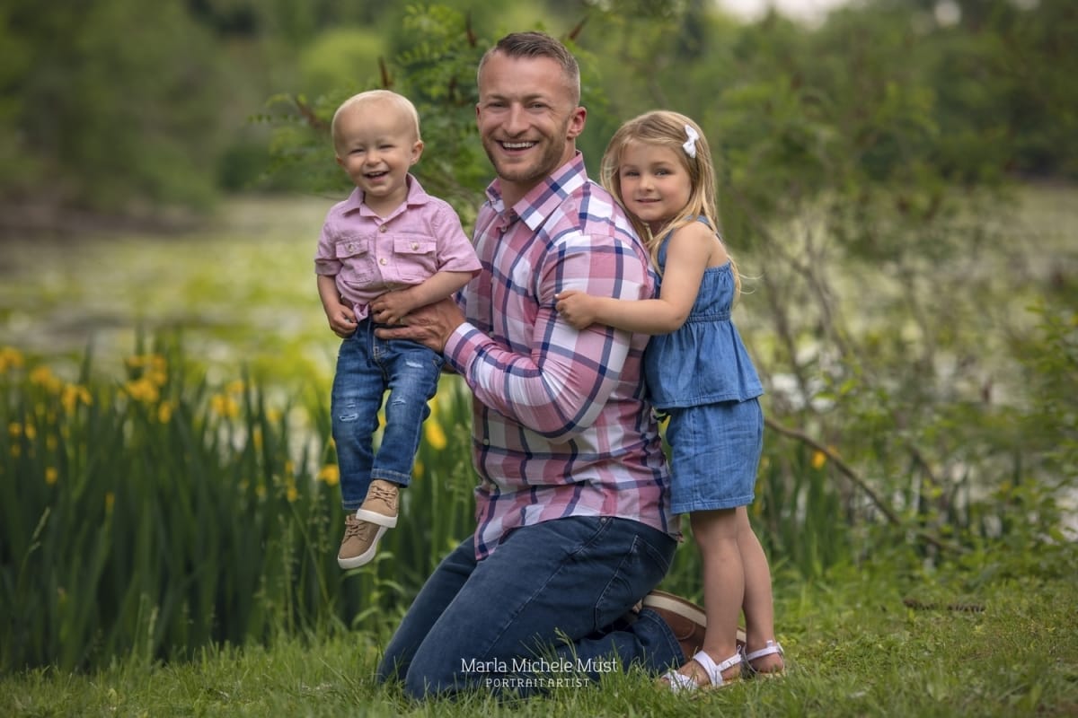 A springtime photoshoot with a father smiling and holding his infant son while his daughter holds him from behind.