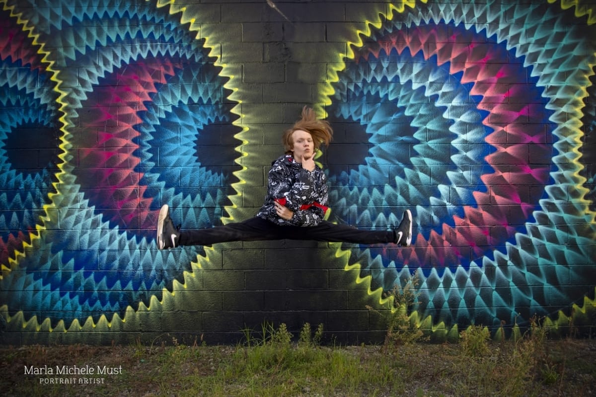 Energetic senior photo jumping and doing splits in front of a Detroit mural