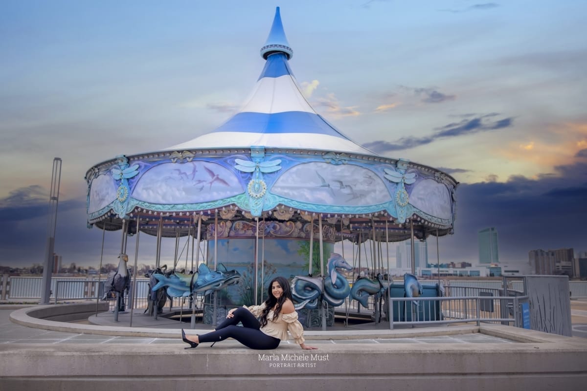 High school senior sits on the ground in front of a Detroit carousel