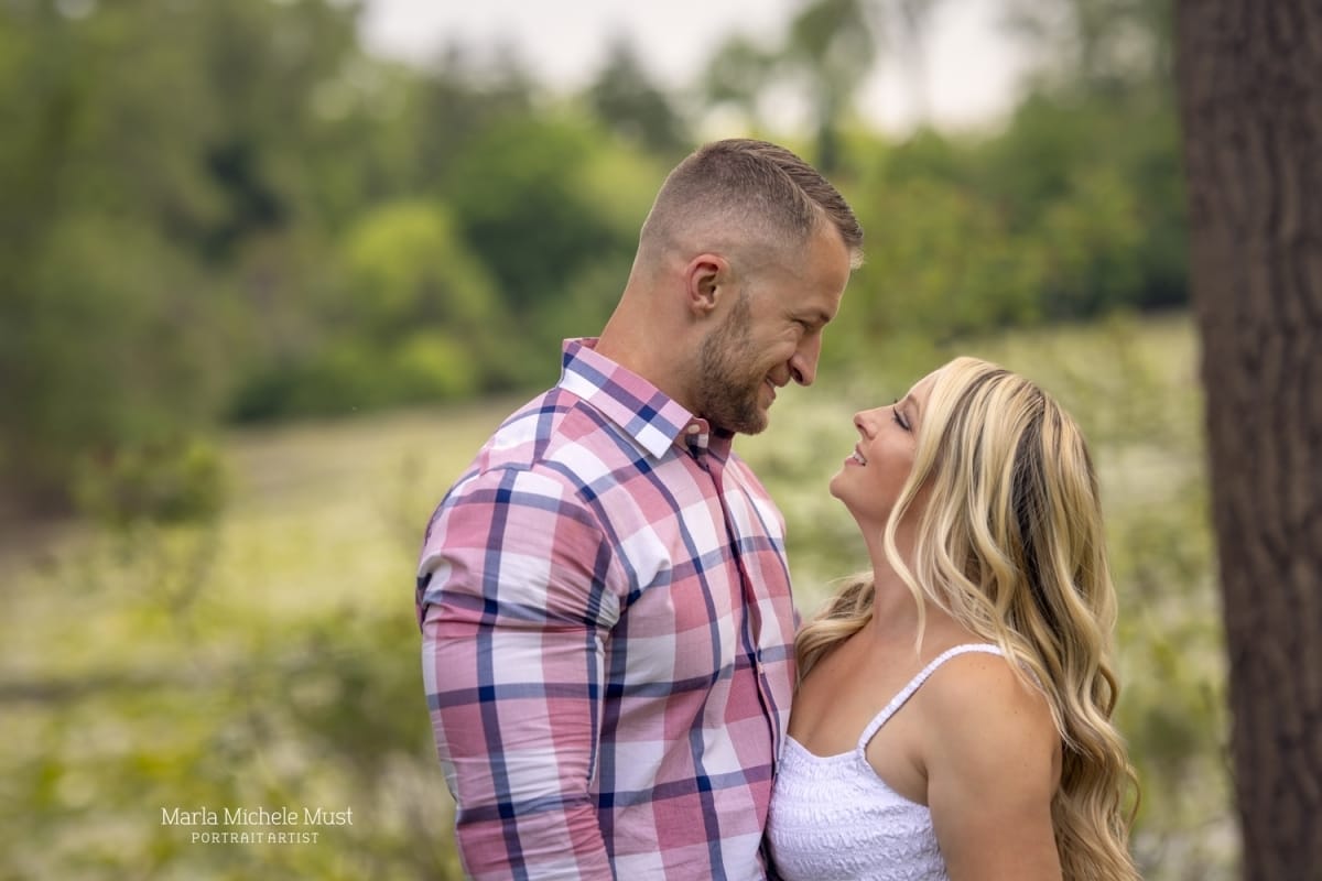 A country photoshoot near Detroit with a woman in a white dress smiling up at her husband wearing plaid.