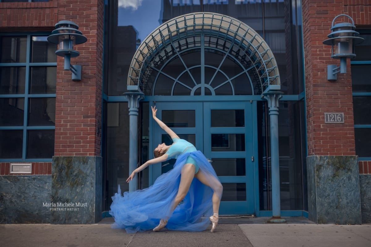 Dancer leaning back in a contemporary pose in front of a blue door in a matching blue dress, photographed by a Detroit-based portrait photographer.