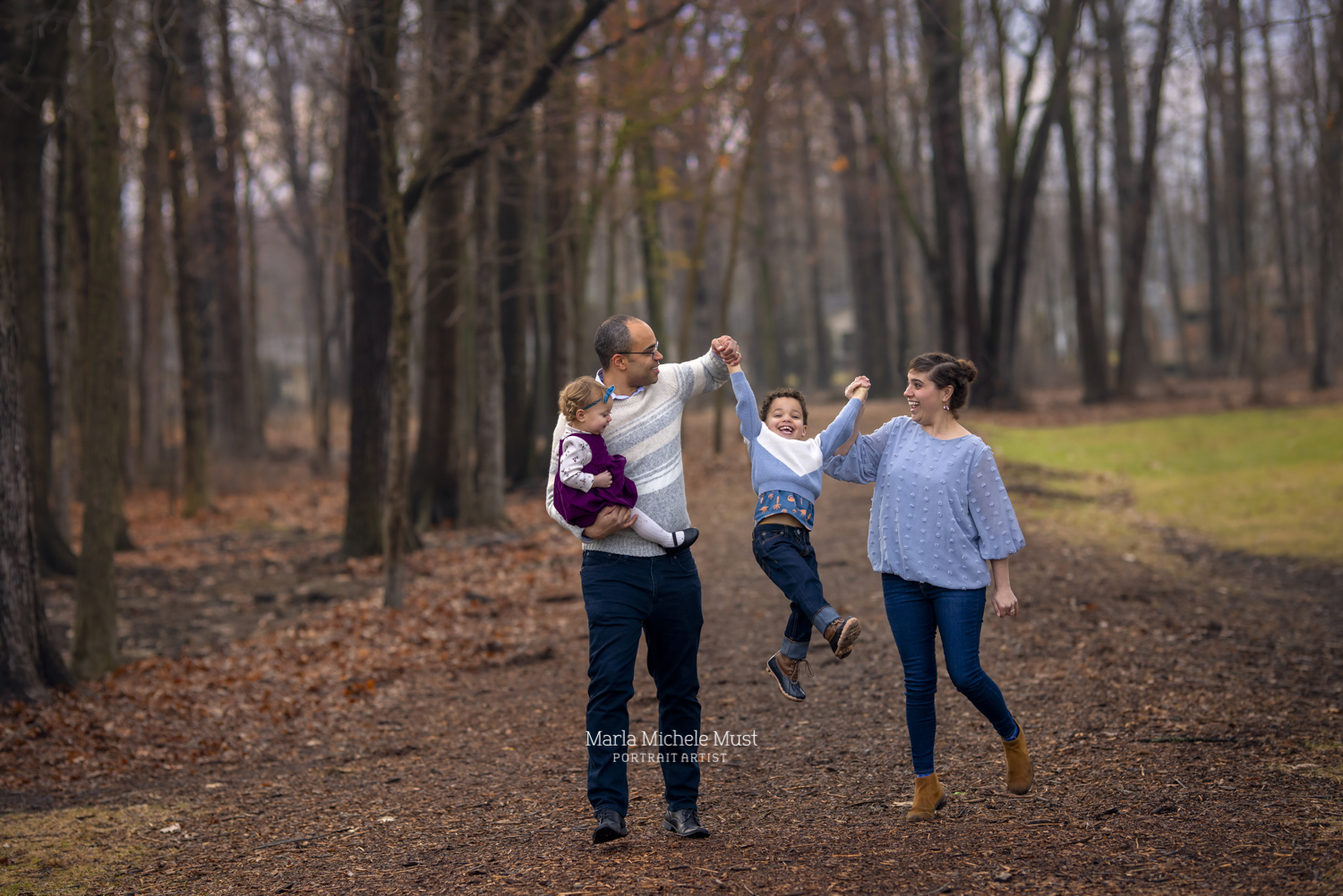 A family of four walk among autumn leaves in the forest as part of a fall family photoshoot near Detroit.