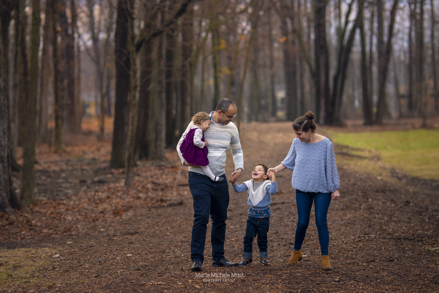 A family of four walk among autumn leaves in the forest as part of a fall family photoshoot near Detroit.