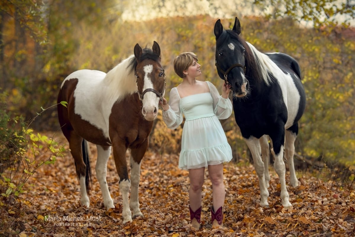 Captivating autumn photo by a Detroit equine photographer, revealing the delight of two horses standing on either side of their owner.