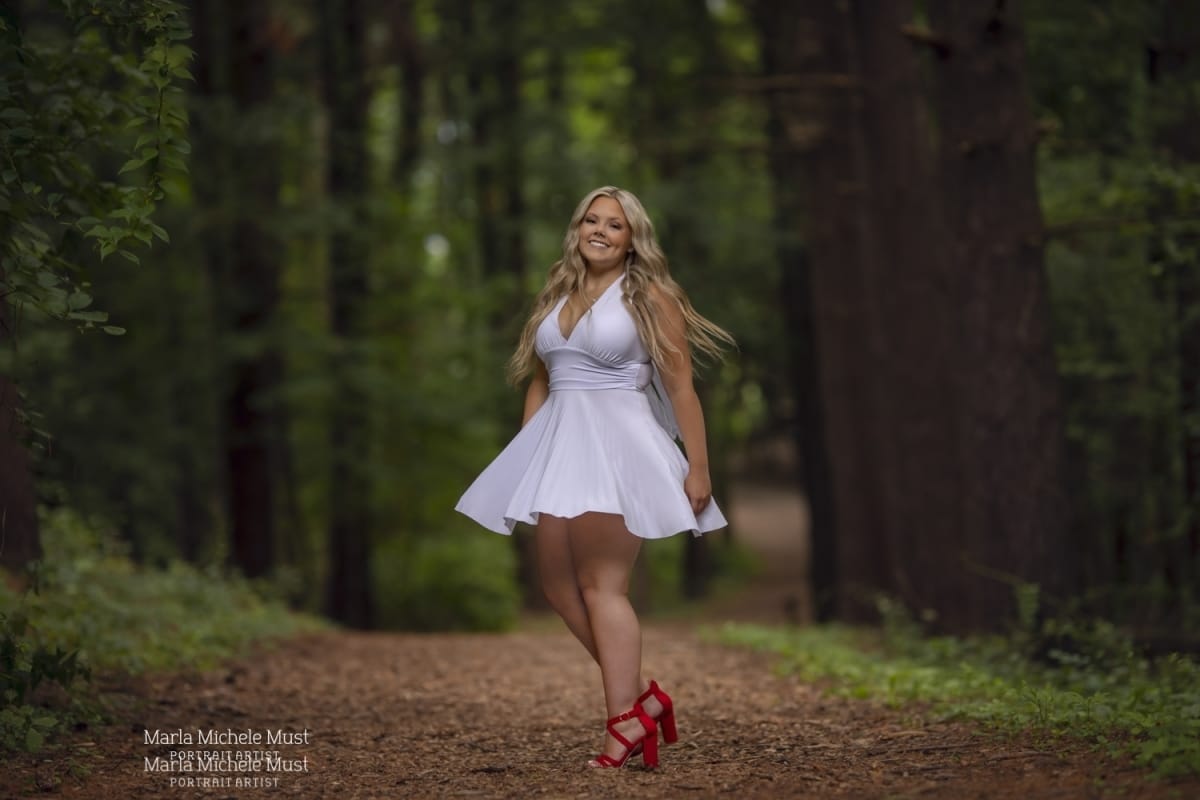 A high school senior poses in her white dress along a Michigan park path during a high school graduation photoshoot