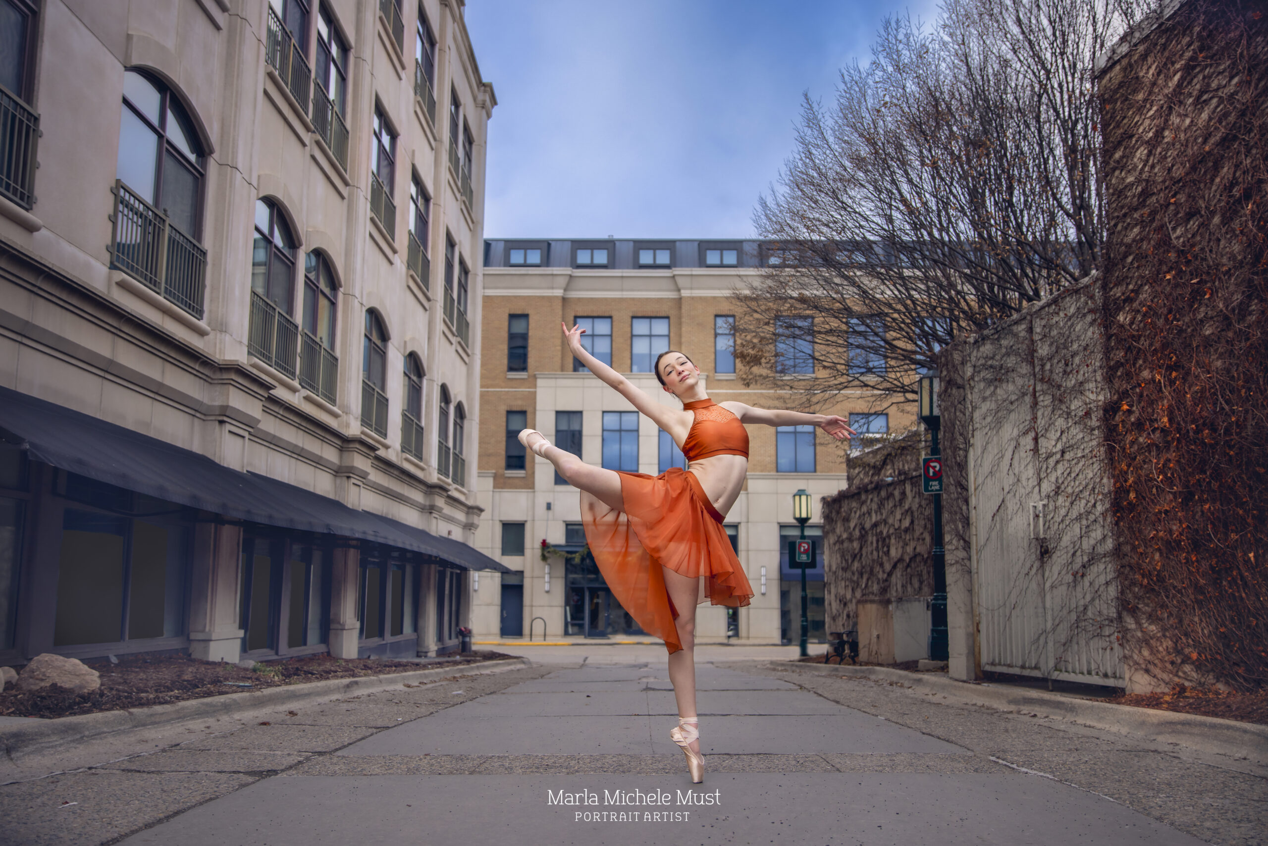 Dancer extends her leg in a poised arabesque pose on a city street, captured by a Detroit-based photographer.