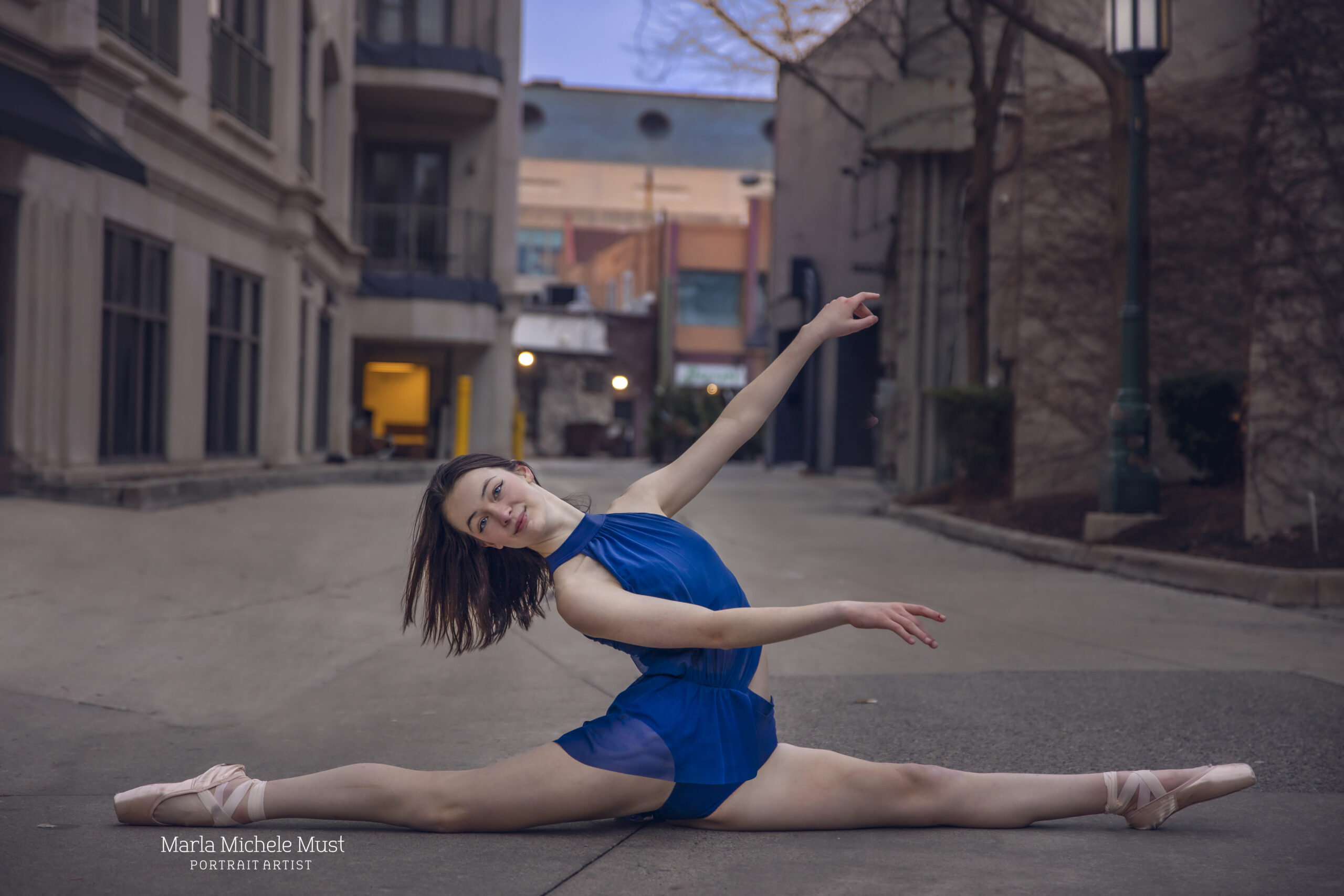 Dancer, wearing a blue outfit on a city street, strikes a contemporary pose in the splits, beautifully photographed by a skilled Detroit dance photographer.