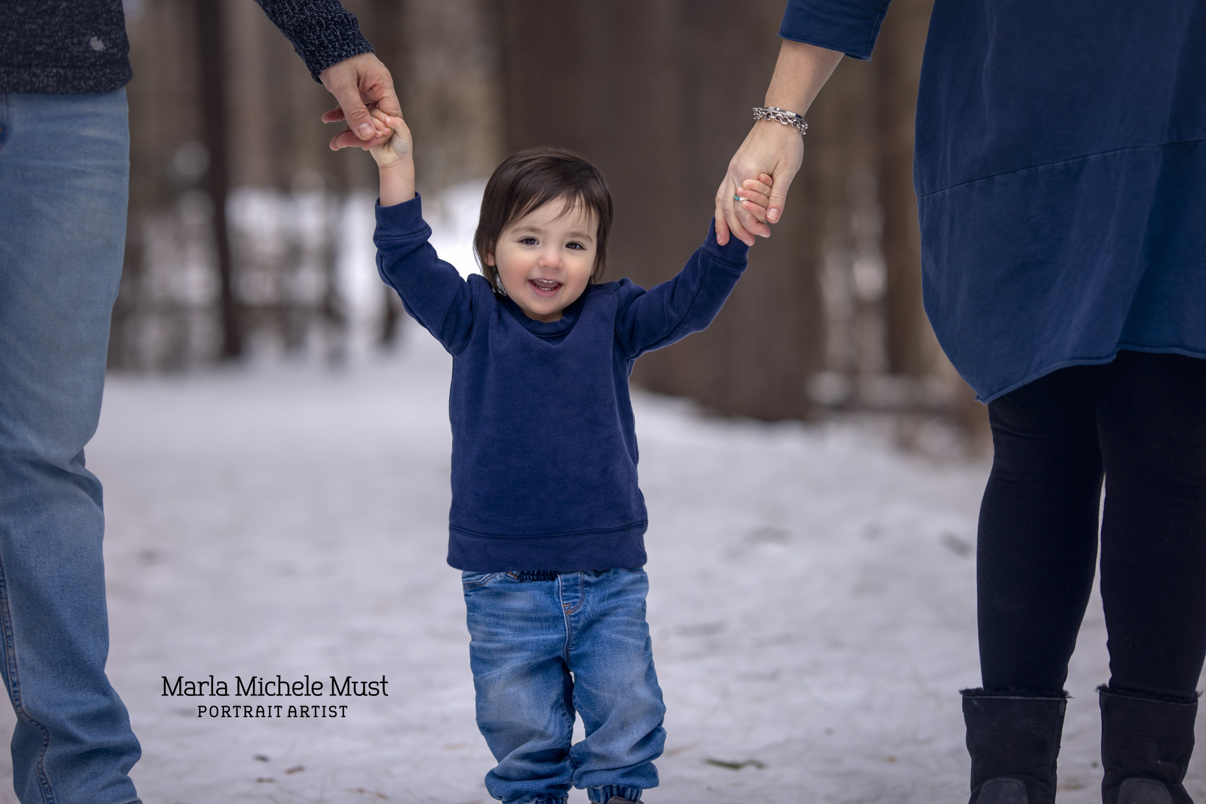 Local family photographer takes photo of aDetroit mother and daughter smiling as the father lifts the toddler in the air, a winter background behind them