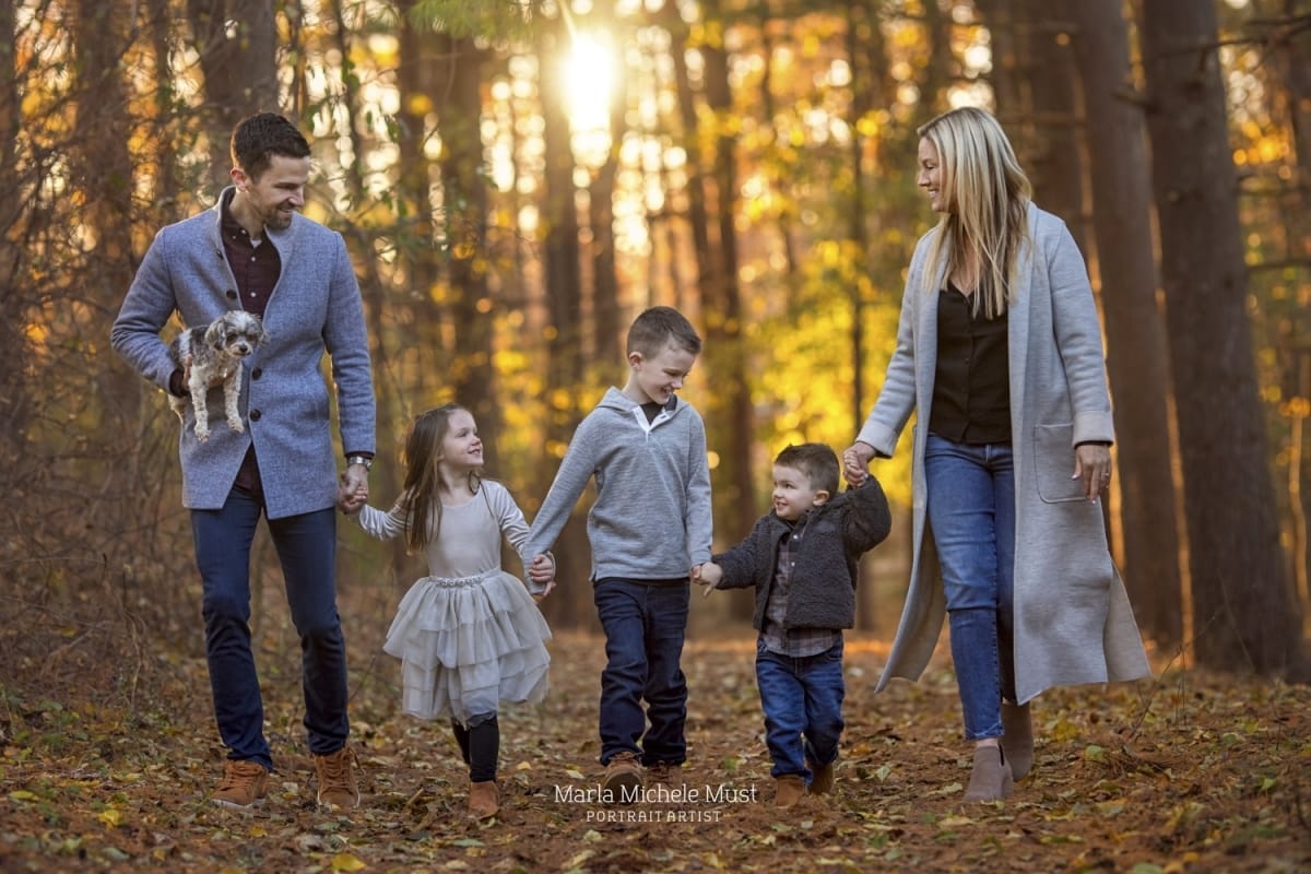 This golden-hour family photo shows a couple holding hands with their three young children in the forests near Grand Rapids.
