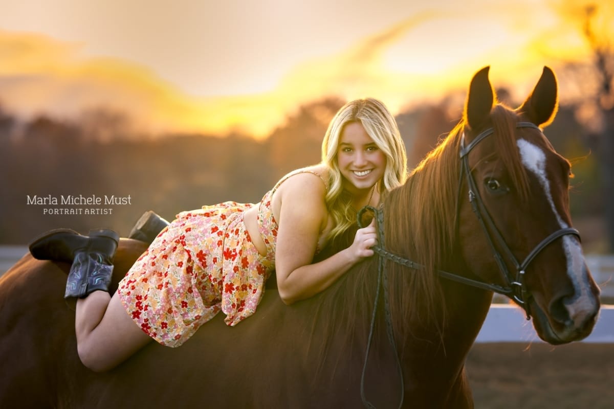 A tender moment in autumn captured by a Detroit equine photographer, conveying a woman lounging on her horse's back amidst sunset hues.
