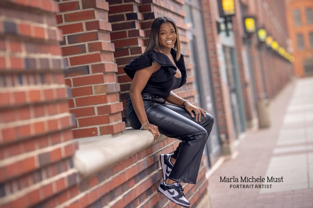 Fashionable senior photo sitting on ledge in Detroit with leather pants captured by a skilled Michigan high school portrait photographer