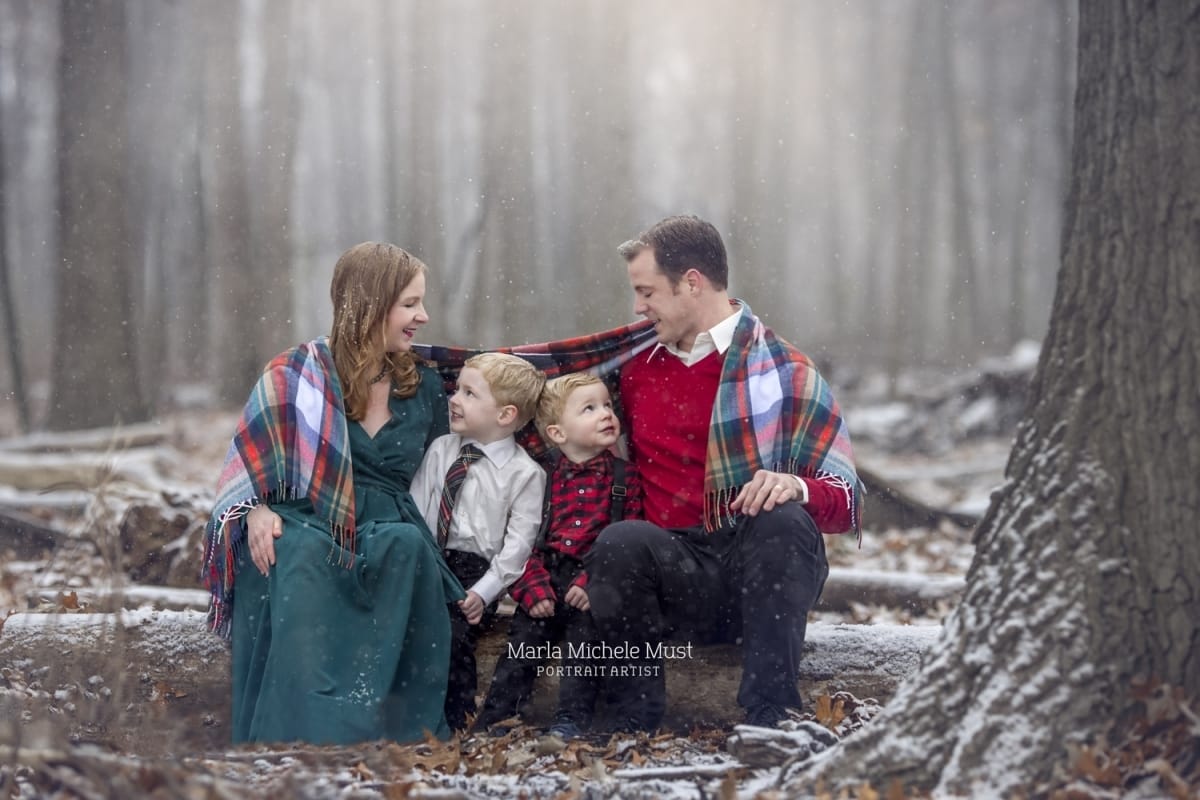 A charming winter photshoot by Detroit photographer of family bundled under blankets in the forest.