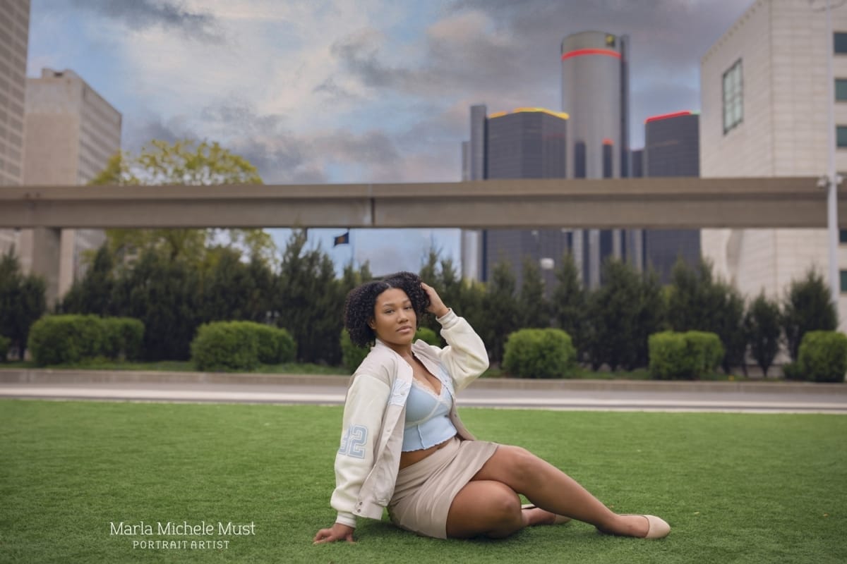 High school graduate photoshoot of a girl sitting on the grass in front of the Detroit skyline