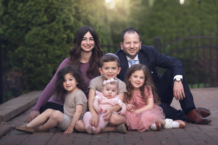 Family wearing tones of pink and blue gracefully sit before a large shrub for a Detroit family photographer.