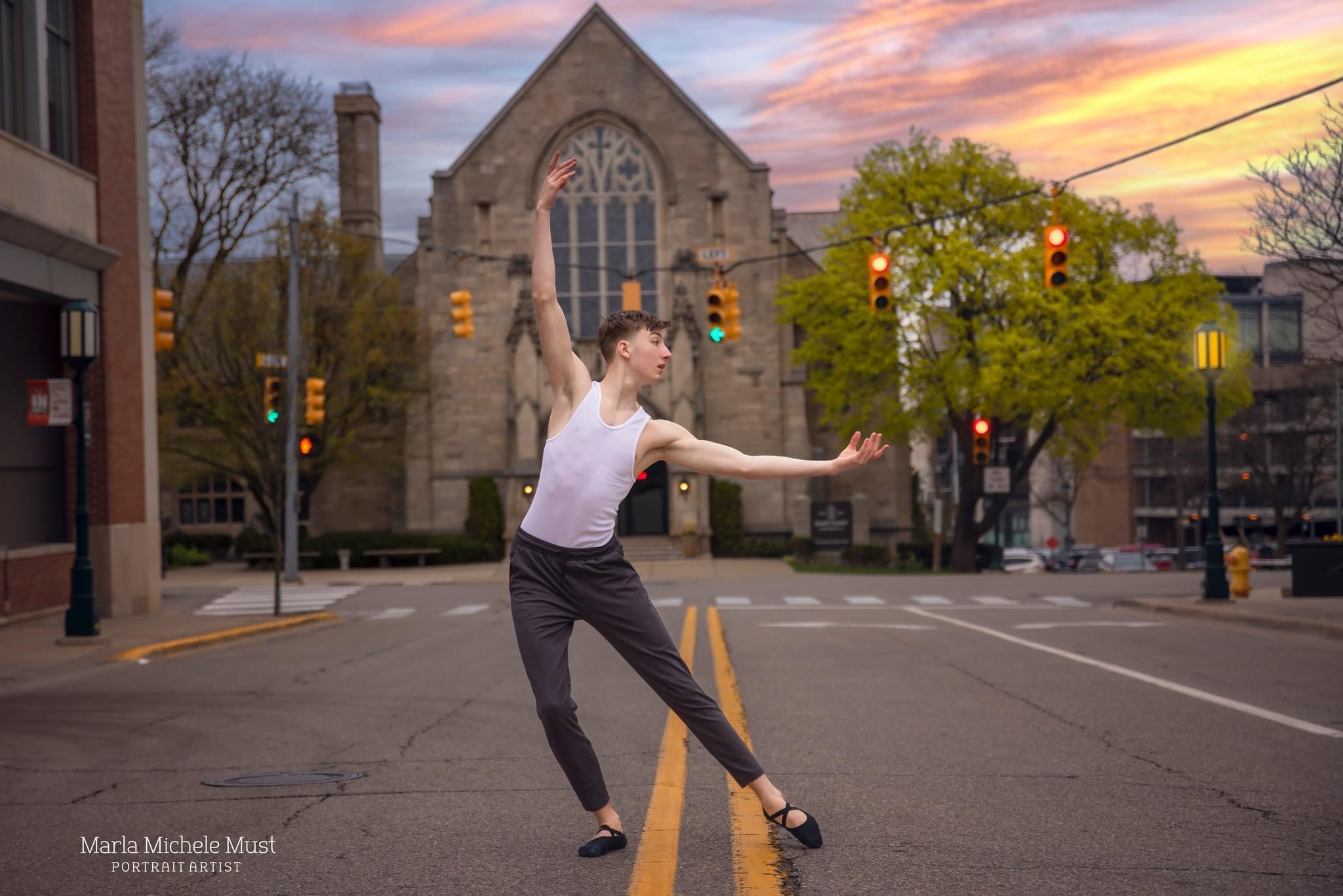 Man poes gracefully leaning to his side in the center of a city street, a brick church in the background, during a dance photoshoot, taken by a Michigan dance photographer.