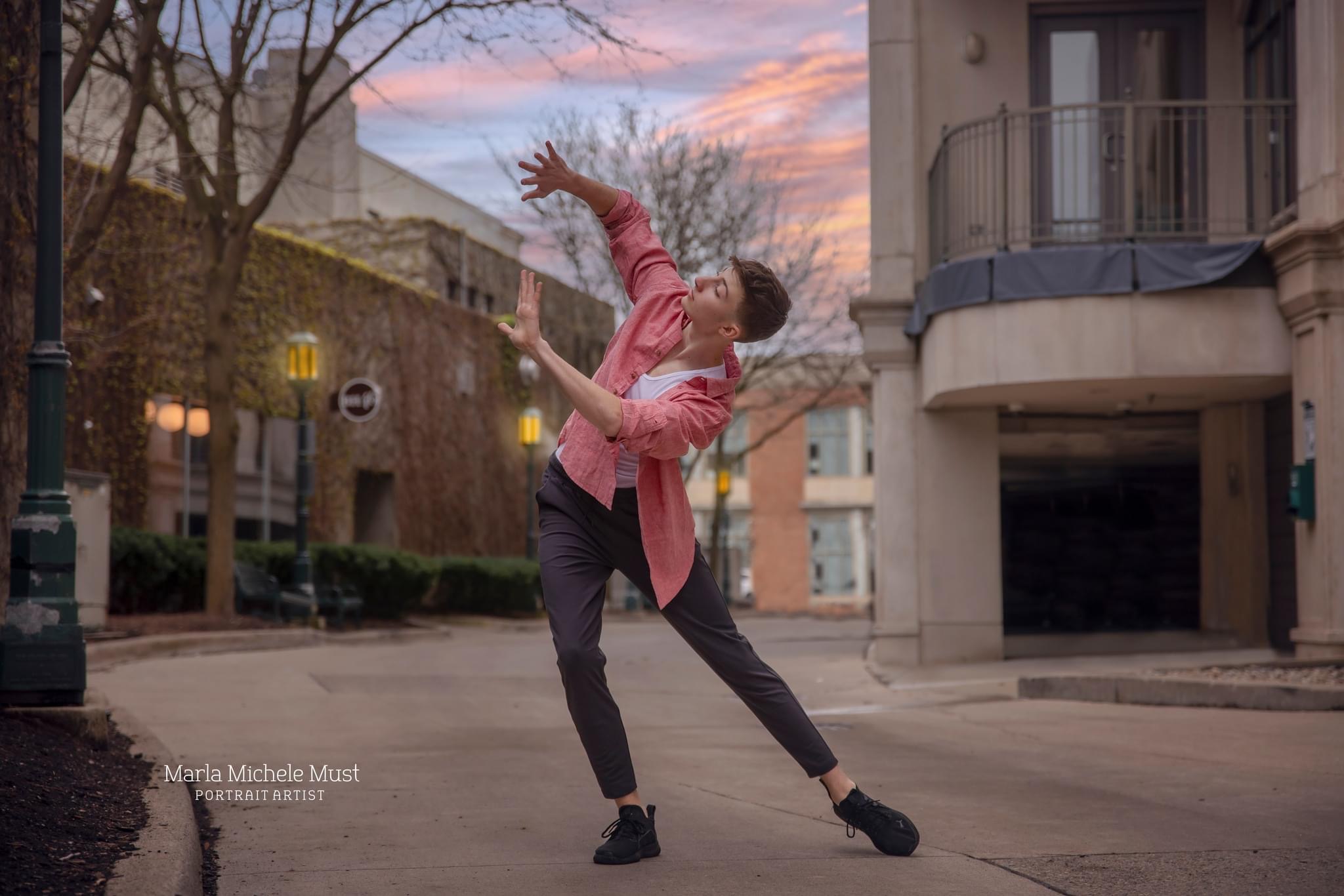 Man in casual clothing poses in a city with his arms shoving out from his sides during a dance photoshoot, taken by a Michigan dance photographer.