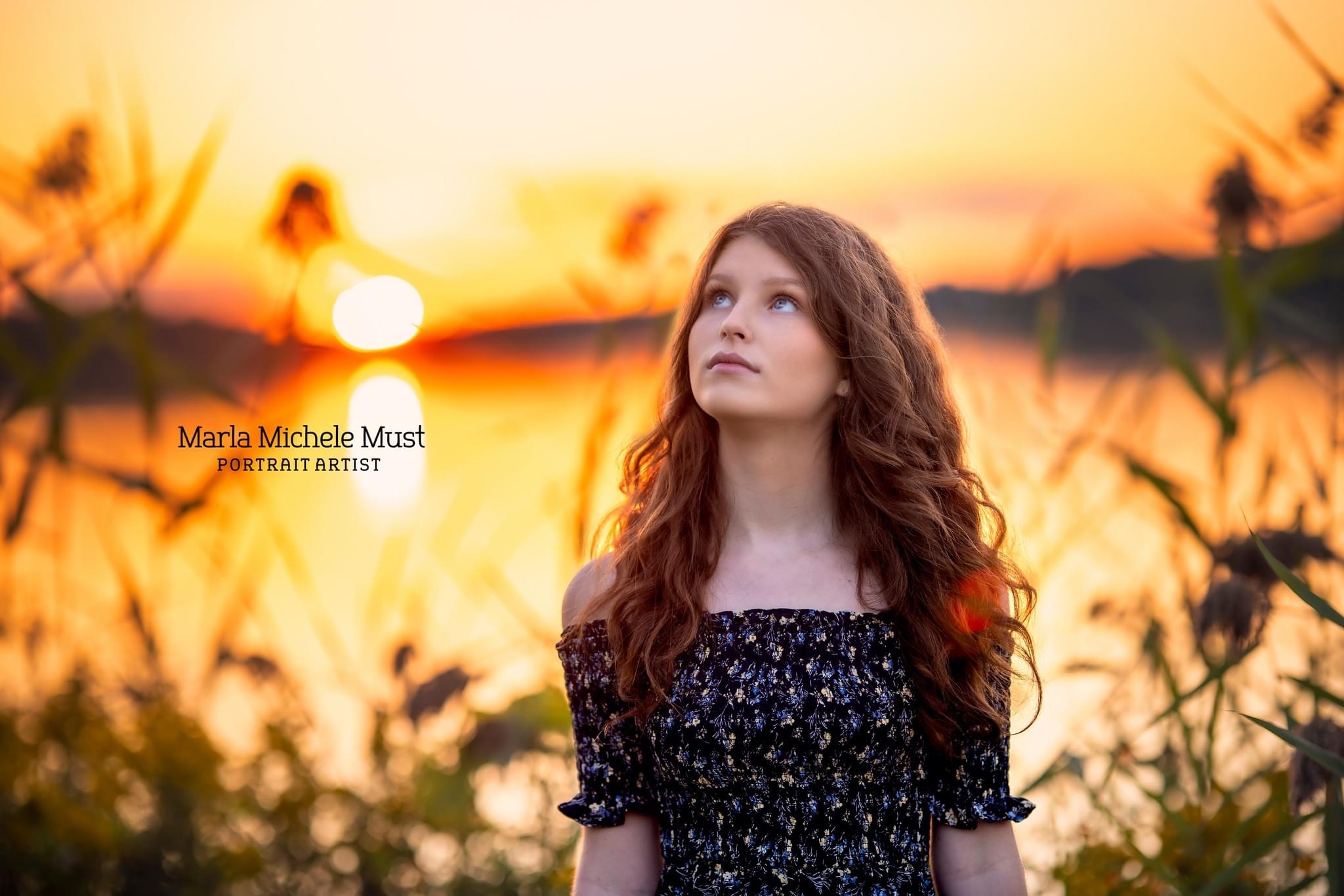 A high schools senior portrait of a girl looking up against the sunset at one of Michigan's great lakes