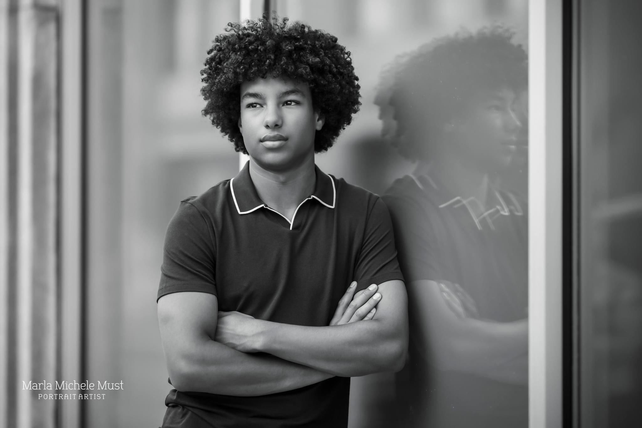 A young man poses for his senior photoshoot while leaning against a chalkboard - the photo by a Detroit senior photo photographer is in black and white