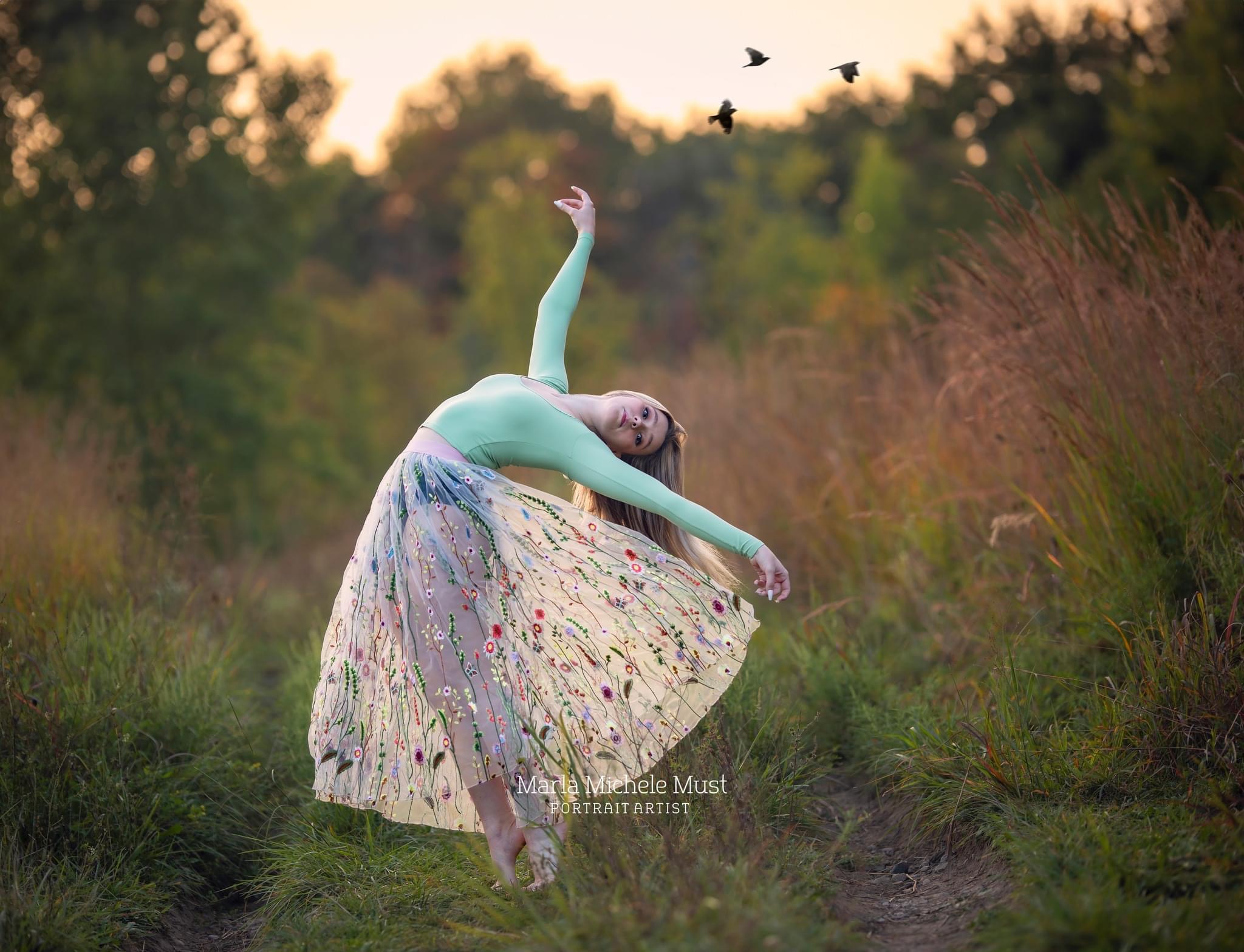 A high school senior strikes a ballerina pose in a field of flowers somewhere in Michigan