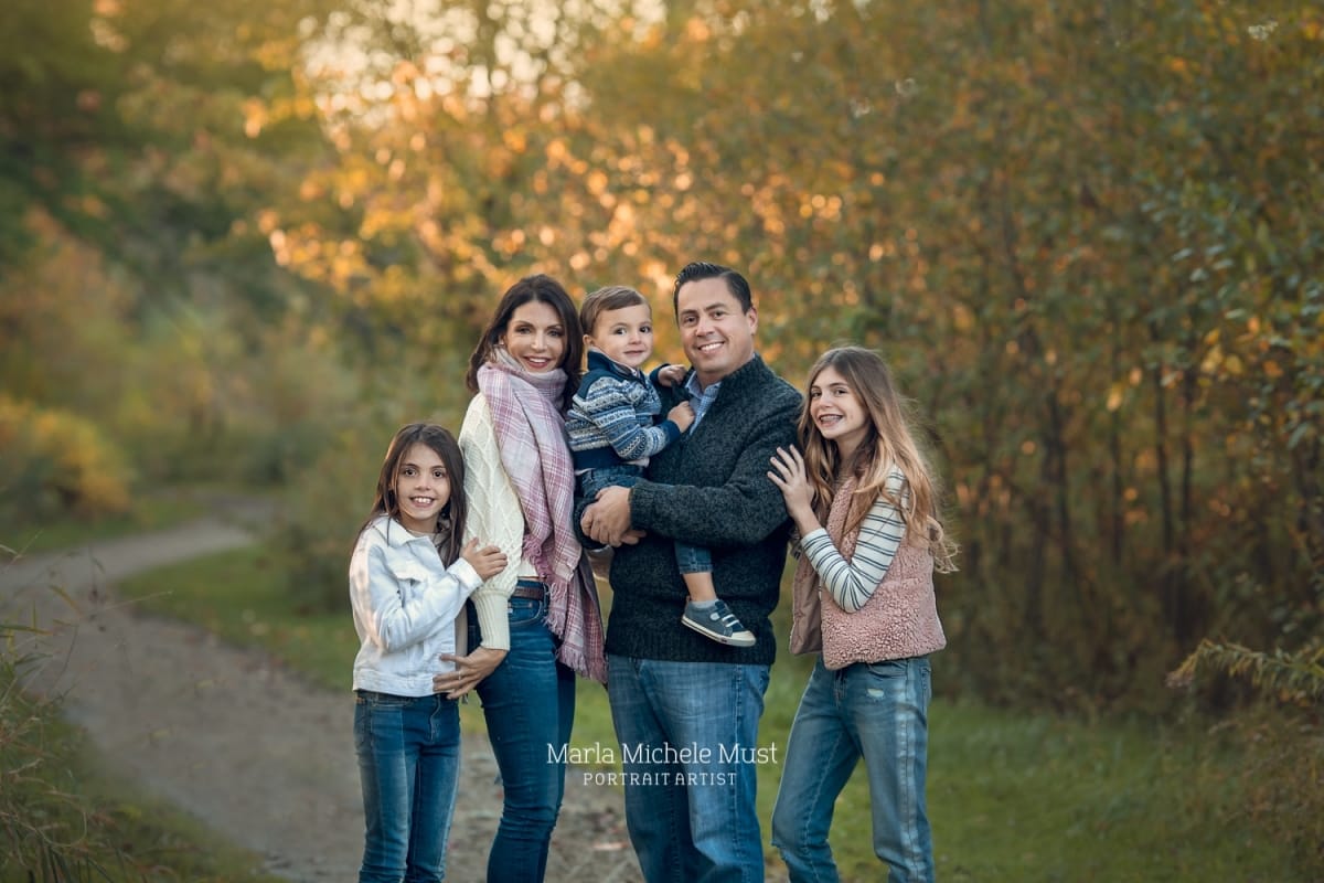 A family of five wearing fall outfits smile for a family photoshoot during golden-hour.